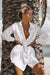 Mujer joven apoyada en una palmera en la playa con una camisa de estilo ibicenco