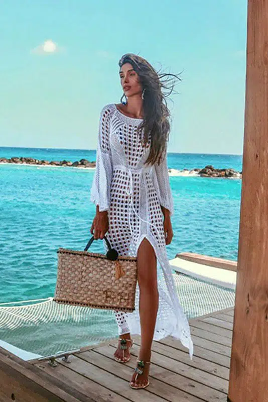 Vestido largo de ganchillo con corte dividido acompanado de un bolso de playa